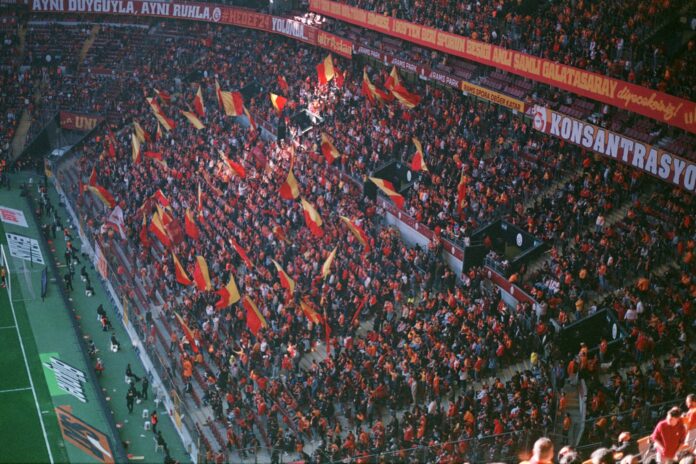 Galatasaray supporters wave red and yellow flags inside Rams Park during a football match.