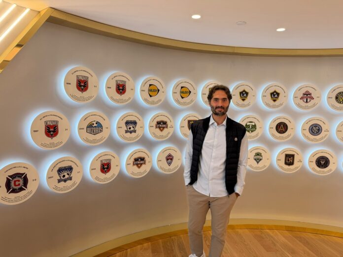 Hamit Altıntop stands in front of the wall at MLS headquarters that displays the league's championship history.