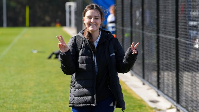Isabel Cabrejas Ruiz smiling beside a football training pitch while making peace signs.
