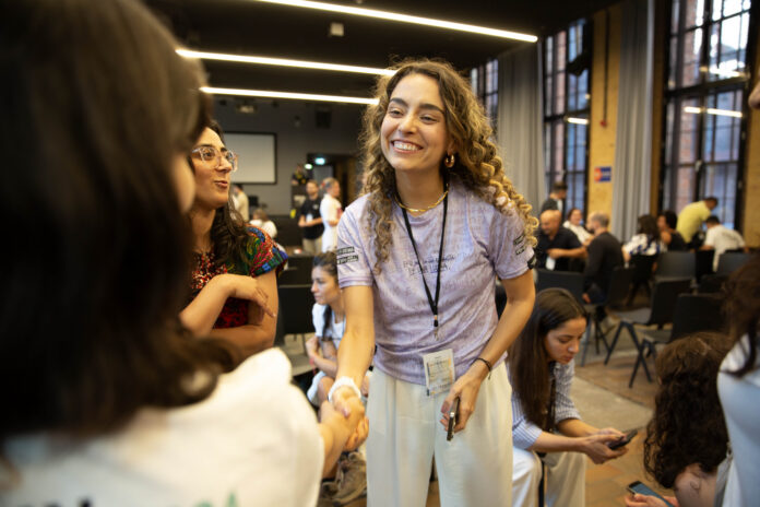 Isabella Echeverri smiles and shakes hands with an attendee at an indoor event.