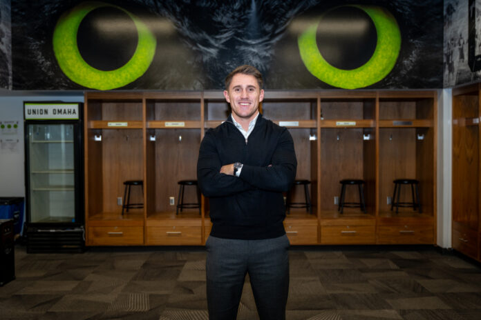 Union Omaha sporting director Jamie Henderson stands in the club’s locker room beneath its owl mural.