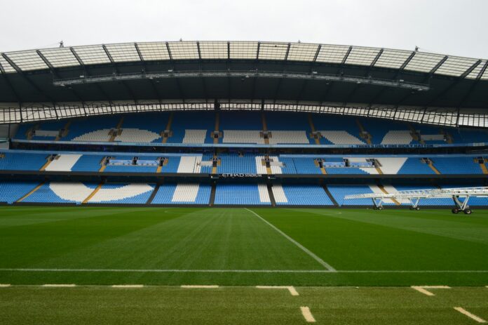 Manchester City’s Etihad Stadium with empty blue and white stands overlooking the pitch.